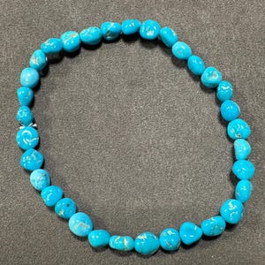May include: A turquoise blue beaded bracelet with a round shape. The beads are all the same size and are strung together on a clear string.