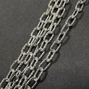 Pode incluir: Um colar de corrente de prata com um padr&atilde;o texturizado, semelhante a um diamante. A corrente &eacute; feita de v&aacute;rias fitas de elos ovais interligados.
