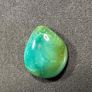 May include: A teardrop-shaped green and blue cabochon gemstone with a smooth, polished surface.