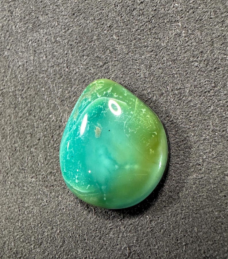 May include: A teardrop-shaped green and blue cabochon gemstone with a smooth, polished surface.