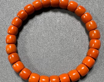 May include: An orange bracelet featuring barrel-shaped beads. The beads are strung together in a circular arrangement. The bracelet's colour is a vibrant orange, and the beads appear to be made of a smooth, polished material. The beads are evenly sized and spaced.