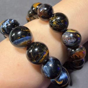 May include: A bracelet featuring large, round beads with a polished, glossy finish. The beads display a mix of dark blue, black, and golden-brown colors, creating a marbled effect. The bracelet is strung together, showcasing the natural stone's unique patterns.