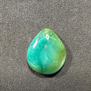 May include: A teardrop-shaped green and yellow gemstone cabochon with a smooth, polished surface.