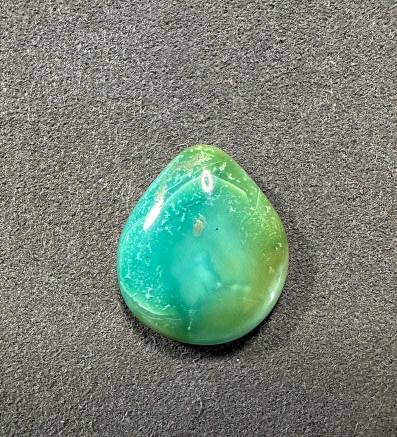 May include: A teardrop-shaped green and yellow gemstone cabochon with a smooth, polished surface.