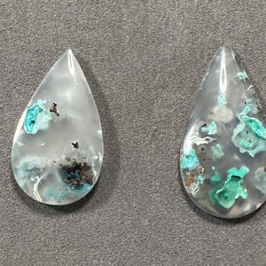 Puede incluir: Cuatro cabujones en forma de l&aacute;grima de cuarzo transparente con inclusiones de minerales verdes y marrones. Los cabujones est&aacute;n pulidos y tienen un acabado liso y brillante.