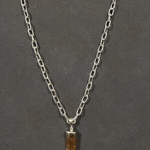 Pode incluir: Um colar de corrente de prata com um pingente de cristal marrom e dourado.