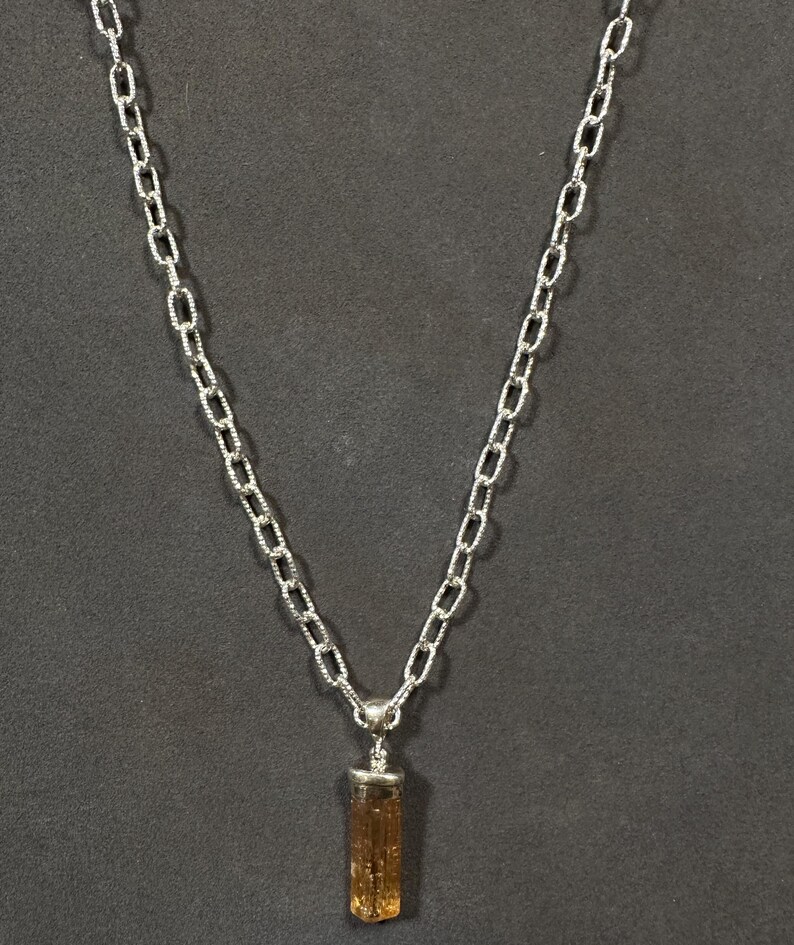Pode incluir: Um colar de corrente de prata com um pingente de cristal marrom e dourado.