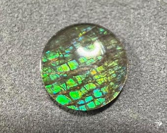 Peut inclure: Une pierre précieuse ovale avec un motif en mosaïque de teintes vertes, bleues et jaunes. La pierre a un fond sombre et une surface polie et réfléchissante. La pierre précieuse est probablement un cabochon.