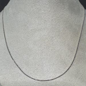 May include: A delicate silver-colored ball chain necklace. The necklace is displayed against a neutral background, highlighting its simple and elegant design. This jewelry piece is suitable for everyday wear.