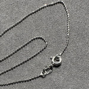 May include: A delicate silver ball chain necklace with a lobster clasp. The clasp is stamped with "ITALY S925". The necklace is displayed on a gray surface.