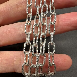 Pode incluir: Close-up de quatro correntes de prata com um padr&atilde;o texturizado em forma de diamante. As correntes s&atilde;o feitas de elos ovais.