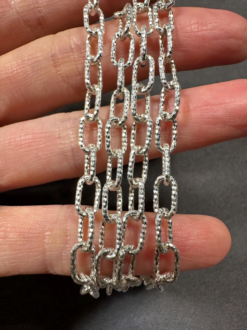 Pode incluir: Close-up de quatro correntes de prata com um padr&atilde;o texturizado em forma de diamante. As correntes s&atilde;o feitas de elos ovais.