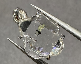 Può includere: Un ciondolo in cristallo esagonale trasparente e sfaccettato con una montatura in argento. Il cristallo contiene inclusiones di minerali verdi e neri.
