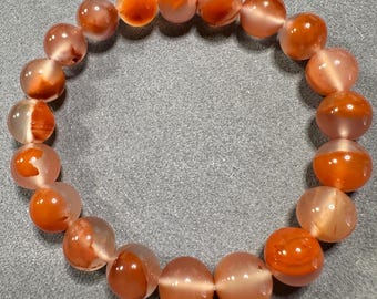 May include: A bracelet made of round, translucent orange and peach-coloured beads. The beads are strung together to form a flexible bracelet. This is a piece of jewellery.