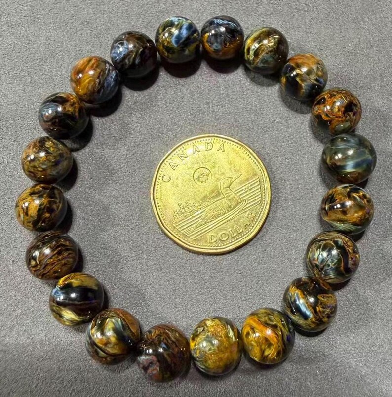 May include: A bracelet made of polished, round tiger eye beads in shades of brown, gold, and blue. A Canadian dollar coin is in the center of the bracelet. The beads are approximately 0.4 inches in diameter.