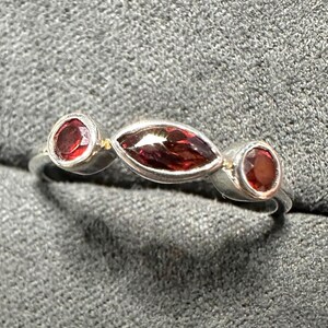 May include: A silver ring featuring three red gemstones. The ring has a central marquise-cut stone flanked by two round stones. The gemstones are set in a silver band, creating a simple yet elegant design.