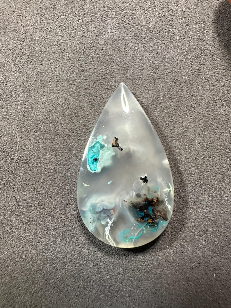 Puede incluir: Un colgante en forma de l&aacute;grima hecho de cuarzo transparente con inclusiones de minerales azules y negros.