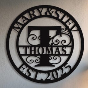 May include: Black metal round sign with the text "Mary & Steve Thomas Est. 2025" and a large letter "T" in the centre.