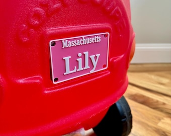 May include: A red toy car with a pink license plate that says "Massachusetts Lily" on it.