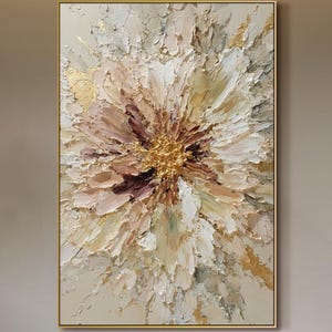 Op de afbeelding: Abstract bloemenschilderij met een gouden lijst. Het kunstwerk heeft een textuur, impasto-stijl met een centrale gouden kern, omringd door bloemblaadjes in wit, beige en bruin. Het schilderij is een groot, rechthoekig canvas.