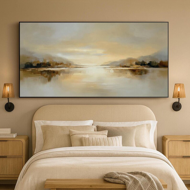 May include: A large rectangular landscape painting with a black frame. The artwork depicts a serene lake scene with muted tones of beige, brown, and gold. The water reflects the sky and distant trees, creating a calming atmosphere. The painting hangs above a bed.