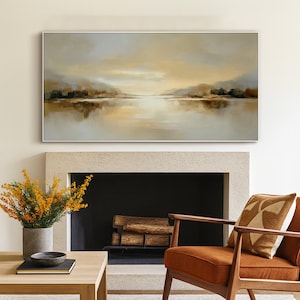 May include: A large rectangular landscape painting with a silver frame. The artwork depicts a serene lake scene with muted tones of beige, brown, and gray. The painting hangs above a fireplace, complementing the warm tones of the room.
