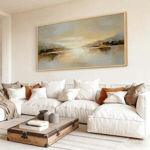 May include: Large landscape painting in a wooden frame. The artwork depicts a serene waterscape with muted tones of beige, brown, and gray. The painting hangs above a white sectional sofa with decorative pillows.