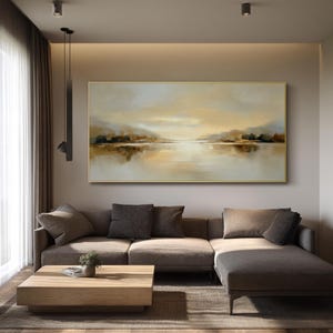 May include: A large rectangular landscape painting with a gold frame. The artwork depicts a serene lake scene with muted tones of beige, brown, and gold. The painting hangs above a brown sectional sofa and a wooden coffee table.