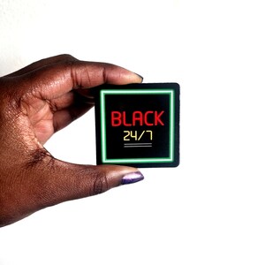 Może przedstawiać: Czarna kwadratowa naklejka z zieloną ramką i tekstem "BLACK 24/7" w kolorze czerwonym i ż&oacute;łtym.