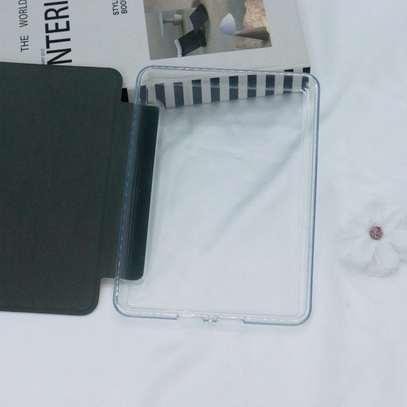 Może przedstawiać: Przezroczyste plastikowe etui na tablet lub czytnik e-book&oacute;w. Etui ma czarną klapkę, kt&oacute;ra składa się na przednią część urządzenia.