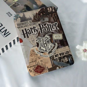 May include: A Harry Potter-themed notebook with a collage design. The cover features the Hogwarts crest, newspaper clippings, and the title "Harry Potter." A "9 3/4" sign is visible.