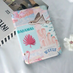 May include: A pink and blue illustrated case with a pink flamingo, a stingray, and coral. The case has the text "Bahamas Sea and Sand" and "life comes in Waves".