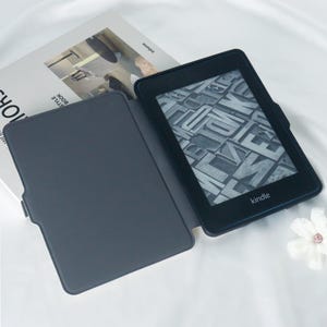 May include: A black Kindle e-reader with a grey case. The e-reader is open and displaying a page of text. The case is closed and has a smooth surface.