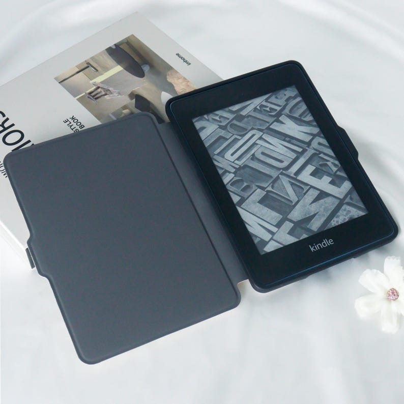 May include: A black Kindle e-reader with a grey case. The e-reader is open and displaying a page of text. The case is closed and has a smooth surface.