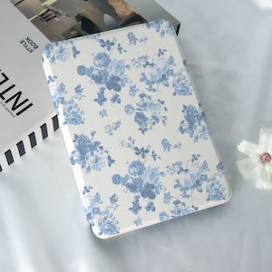 May include: A white and blue floral patterned case for an e-reader. The case has a soft, textured surface and a subtle sheen.