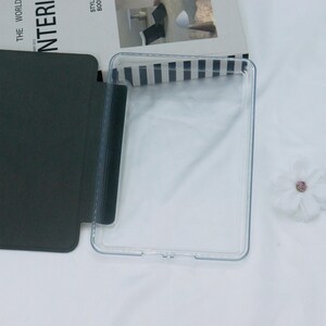 May include: A clear plastic case for a tablet or e-reader. The case has a black flap that folds over the front of the device.