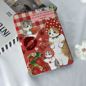 May include: A red and white checkered background with two white cats wearing strawberry hats. The cats are surrounded by strawberries, hearts, and stars. The text "Just like the strawberry life is full of sweetness and surprises." is printed on the top of the image.