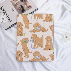 May include: A tablet case featuring a repeating pattern of cartoon golden retrievers in various poses. The dogs are light brown with blue and green accents, set against a light beige background. Some dogs have a blue leash or a green collar.