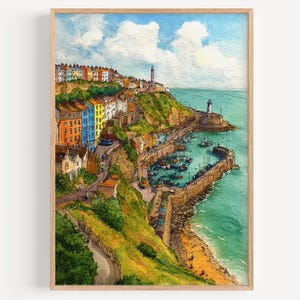 May include: Watercolour painting of a coastal town with brightly coloured buildings on a cliff. A lighthouse stands at the edge, overlooking a harbour filled with boats. The artwork is framed in a light-coloured wooden frame.
