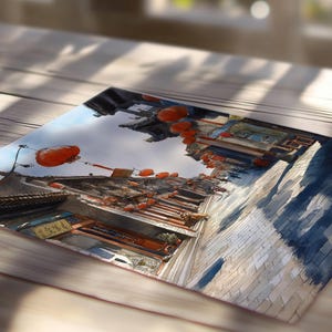 May include: Watercolor painting of a traditional Asian street scene. The artwork depicts buildings with red lanterns, a cobblestone street, and a cloudy sky. The painting is displayed on a wooden surface.