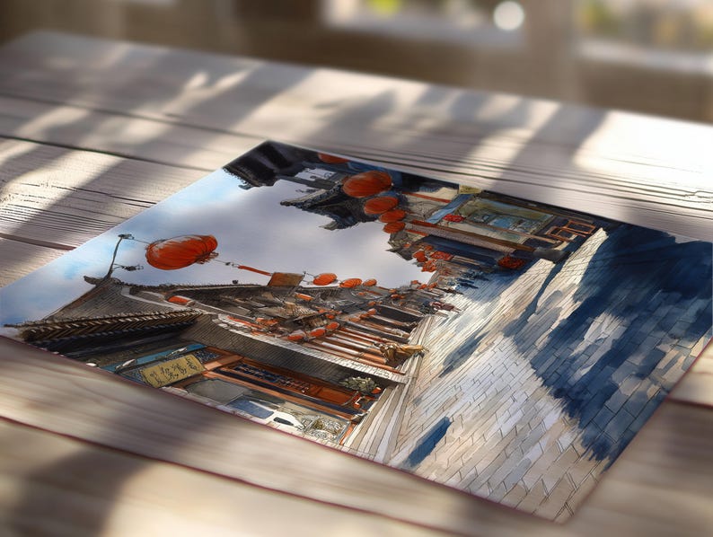 May include: Watercolor painting of a traditional Asian street scene. The artwork depicts buildings with red lanterns, a cobblestone street, and a cloudy sky. The painting is displayed on a wooden surface.