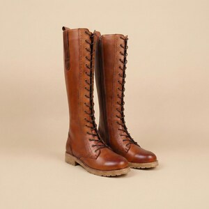 Peut inclure: Une paire de bottes hautes en cuir marron avec un la&ccedil;age et une fermeture &eacute;clair lat&eacute;rale. Les bottes ont un style classique et vintage avec un petit talon et une semelle textur&eacute;e. Les bottes mesurent environ 40 cm de haut.
