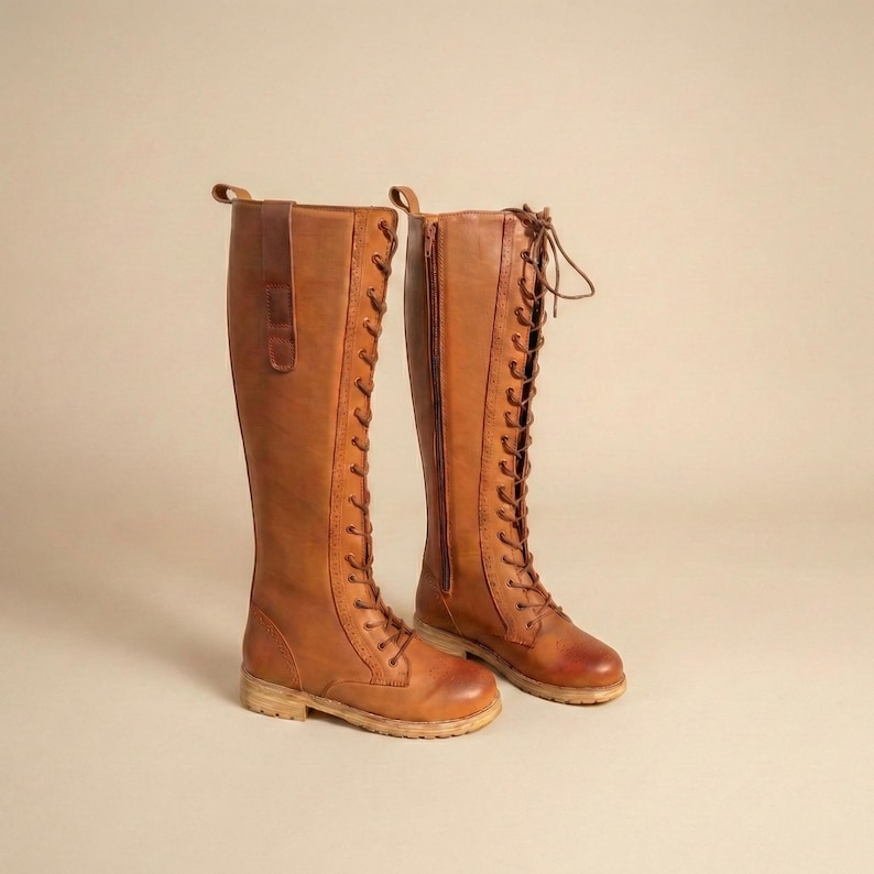 Peut inclure: Une paire de longues bottes en cuir marron, arrivant au genou. Les bottes ont un la&ccedil;age, une fermeture &eacute;clair lat&eacute;rale et une petite languette en haut. Les semelles sont de couleur beige clair.