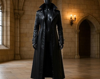 May include: A long, black leather coat with a wide collar and button closure, displayed on a mannequin. The coat reaches to the ankles and is paired with black gloves and boots. The setting is a stone-walled room with arched doorways and a window.