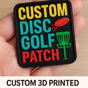 May include: A black, square 3D-printed patch with the words "CUSTOM DISC GOLF PATCH" in yellow, teal, and red. The patch features a red disc and a green disc golf basket. The text "CUSTOM 3D PRINTED DISC GOLF PATCH" is below the patch.