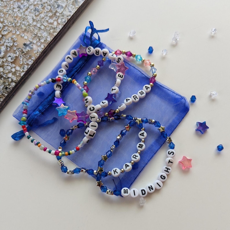 Several Midnights themed Taylor Swift friendship bracelets on a blue organza gift bag, featuring songs and lyrics from the Midnights album including Karma, Midnights, Glitch, All the stars aligned.