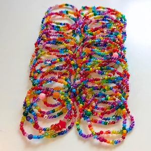 Peut inclure: Une collection de bracelets circulaires composés de petites perles en verre multicolores formant un arc-en-ciel. Les bracelets présentent diverses formes de perles, notamment rondes, translucides et opaques, avec quelques petites breloques en forme d'étoile.