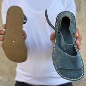 Peut inclure: Deux sandales en cuir, l'une à semelle plate et l'autre à talon avec une bride. Les deux sandales sont bleues.