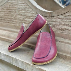 Puede incluir: Un par de zapatos de cuero burdeos de vestir sin cordones con suela cosida de color marr&oacute;n claro.