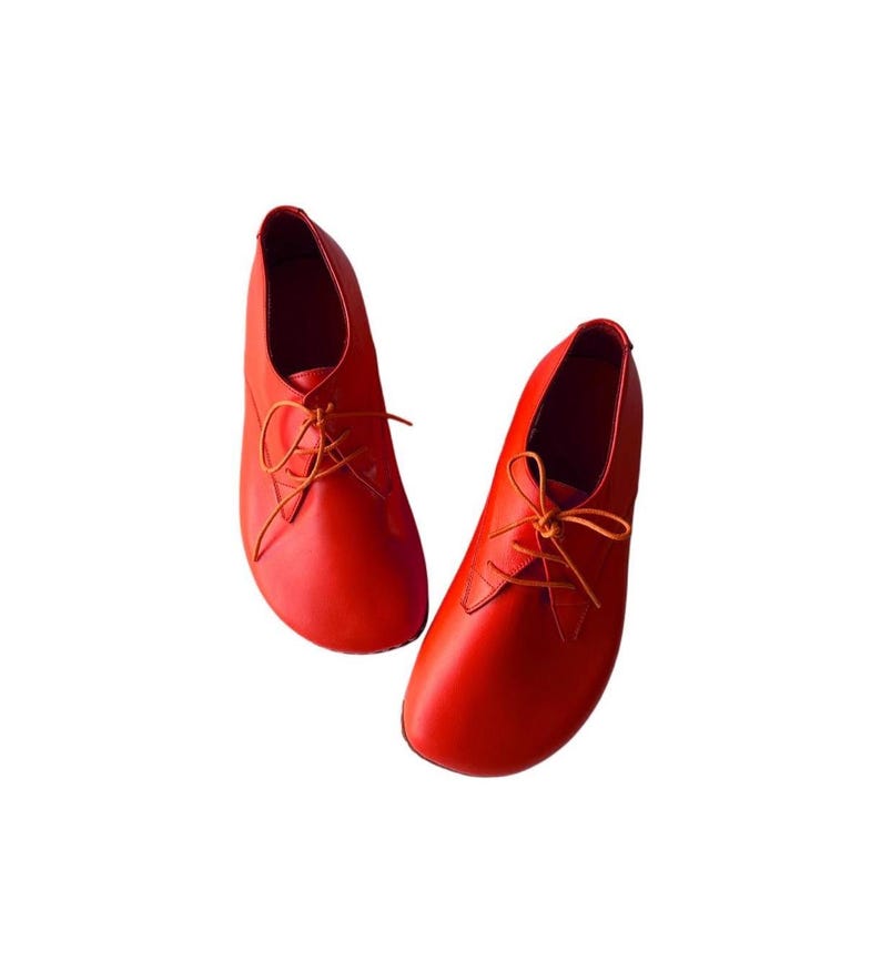 May include: A pair of vibrant red lace-up shoes featuring a smooth, rounded toe design and thin matching red laces. The shoes have a low-cut silhouette with a clean, minimalist construction and a solid, uniform color throughout the entire exterior.